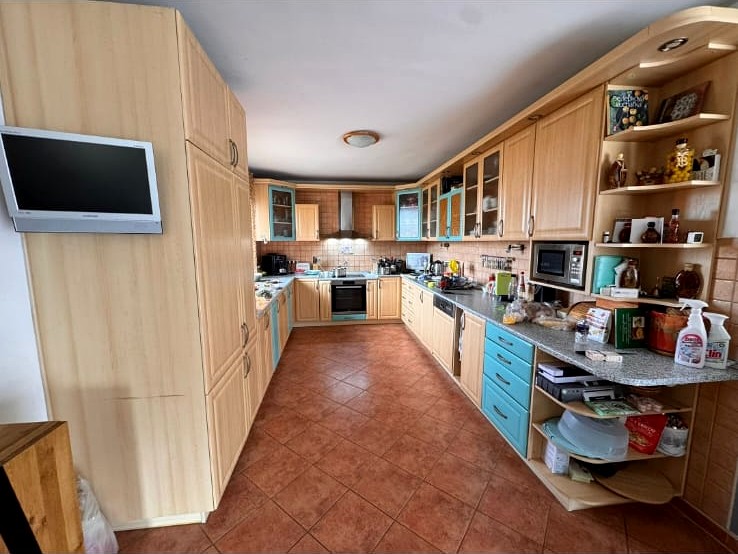 Before: a dated kitchen with light wood cabinetry, teal accents and terracotta tile floor